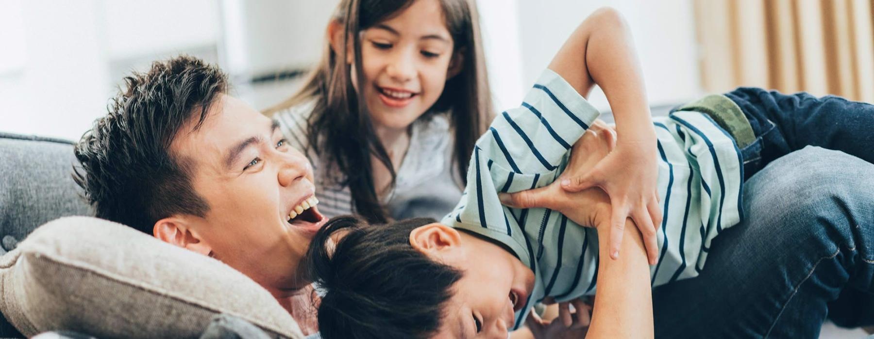 father plays on a couch with his young children